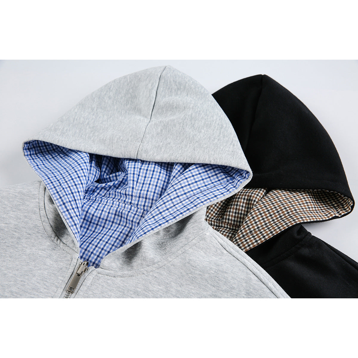 Close-up of gray and black zip-up hoodie hoods with blue and brown plaid linings.