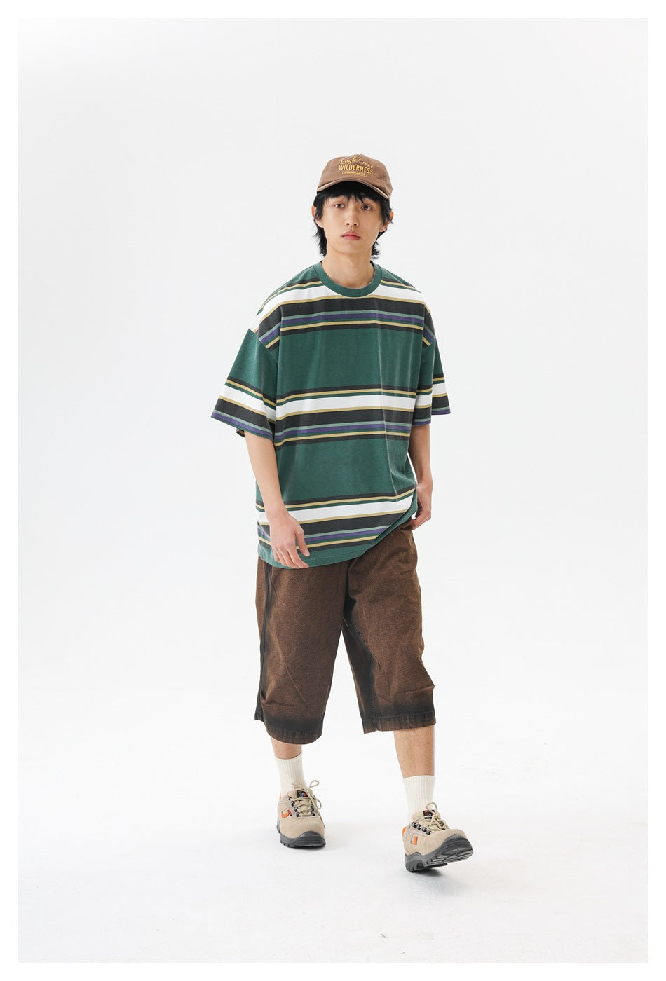 Model wearing an oversized forest-green T-shirt with broad white and narrow charcoal, purple, and tan horizontal stripes.
