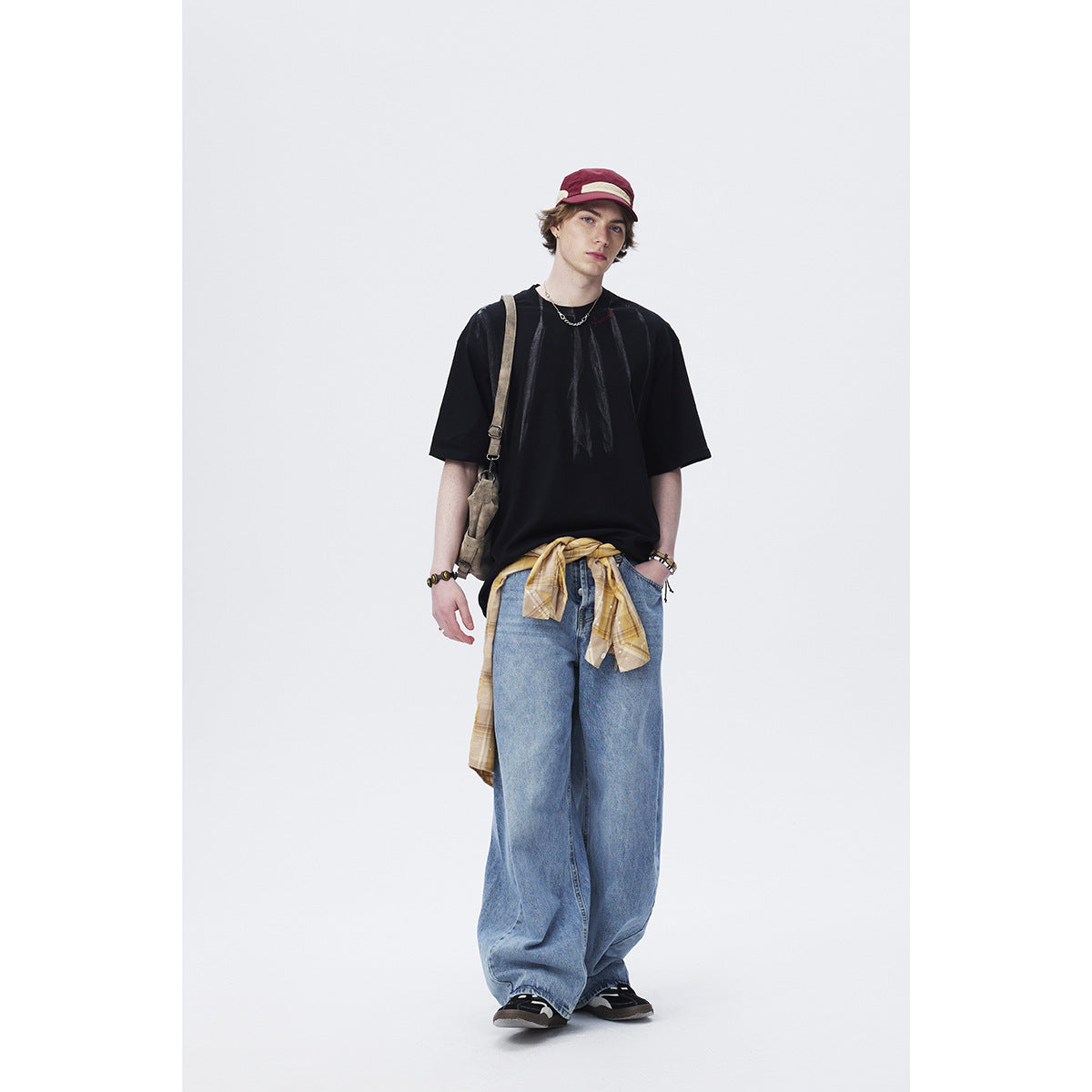 Front view of a model wearing an oversized black T-shirt with a subtle vertical graphic, blue wide-leg jeans, and a plaid