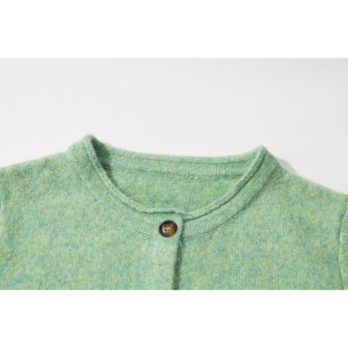 Close-up of a mint green and yellow-mottled cardigan neckline with a dark brown button.