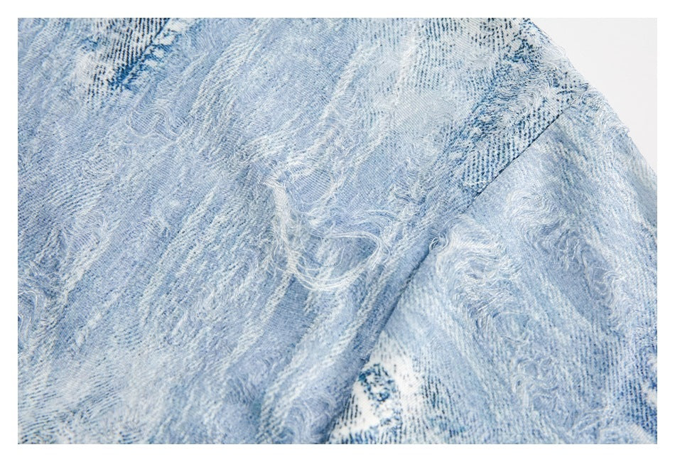 Pale blue patterned garment close-up showing a diagonal stitched seam and frayed distressed patches.