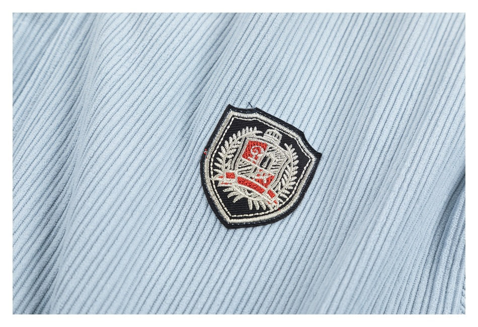 Close-up of a black, cream, and red embroidered shield patch on pale blue ribbed fabric.