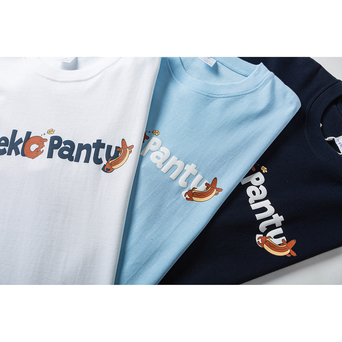 White, light blue, and navy T-shirts with large playful lettering and cartoon food graphics.