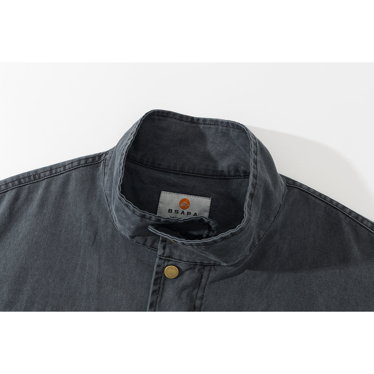 Close-up of a charcoal jacket's stand collar, brass snap, and inner brand label.
