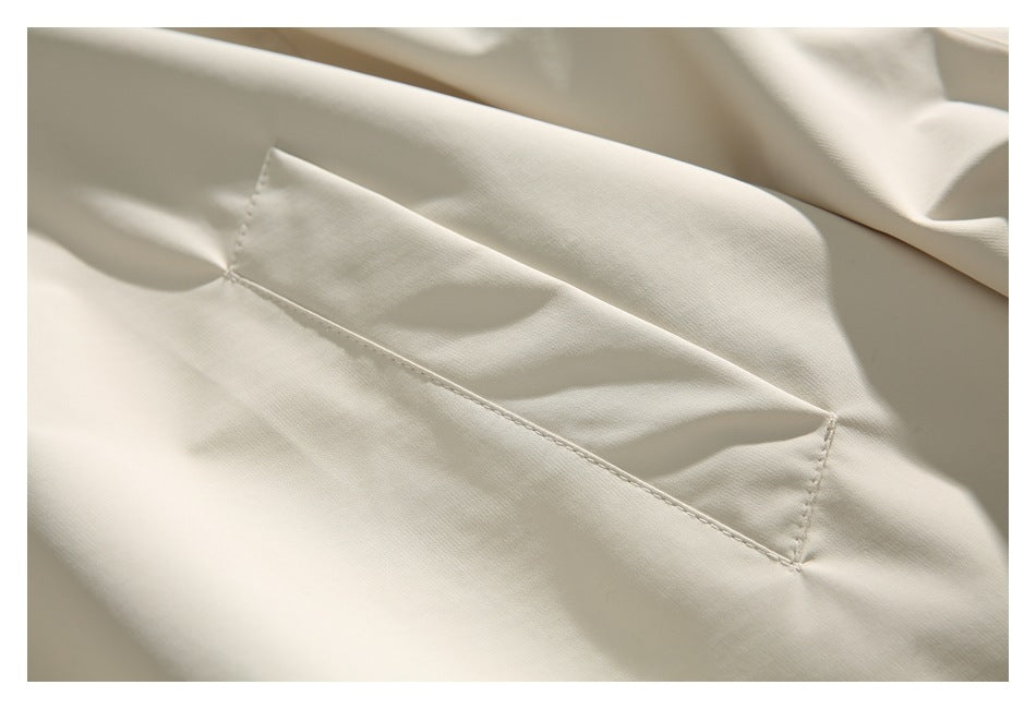 Close-up of an ivory coat's stitched pocket and smooth fabric.