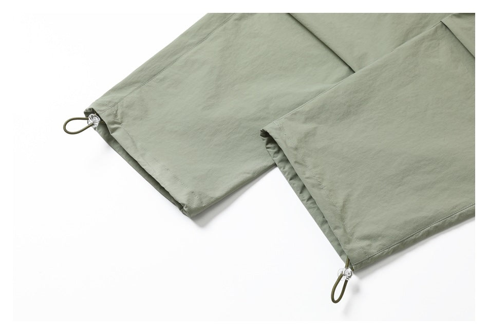 Close-up of sage-green pant hems with small looped drawcords and toggle adjusters.