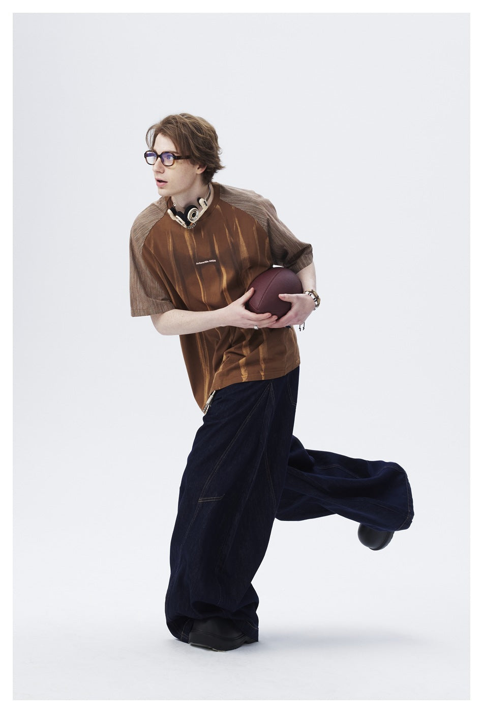 Model wearing a brown short-sleeve shirt with gray striped raglan sleeves and vertical accents, paired with wide dark jeans.