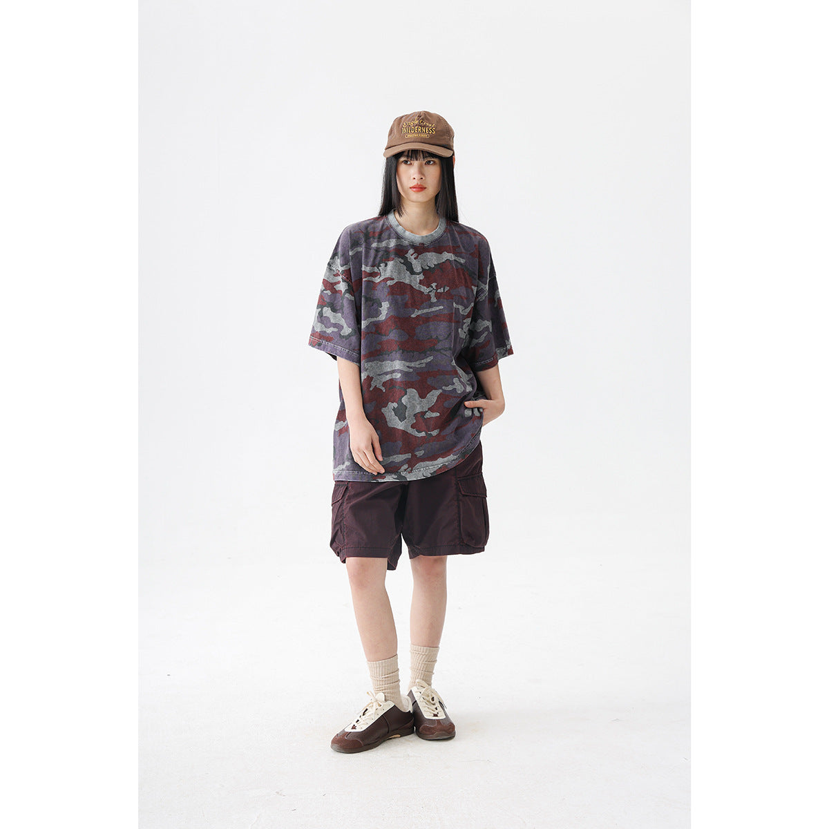 Model wearing an oversized burgundy, gray and charcoal camouflage T-shirt with dark burgundy shorts.