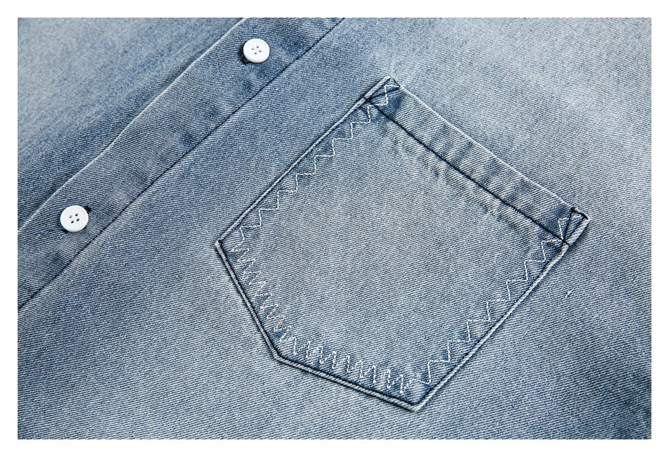 Close-up of a square chest pocket with zigzag stitching and white buttons on a light blue denim shirt.