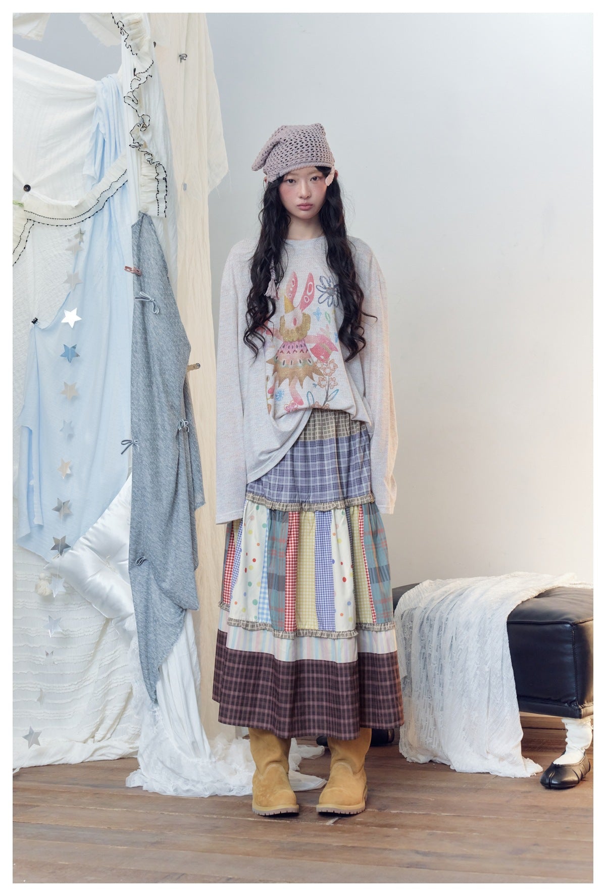 Full-length model in a colorful tiered patchwork skirt with an illustrated long-sleeve top and knit cap.