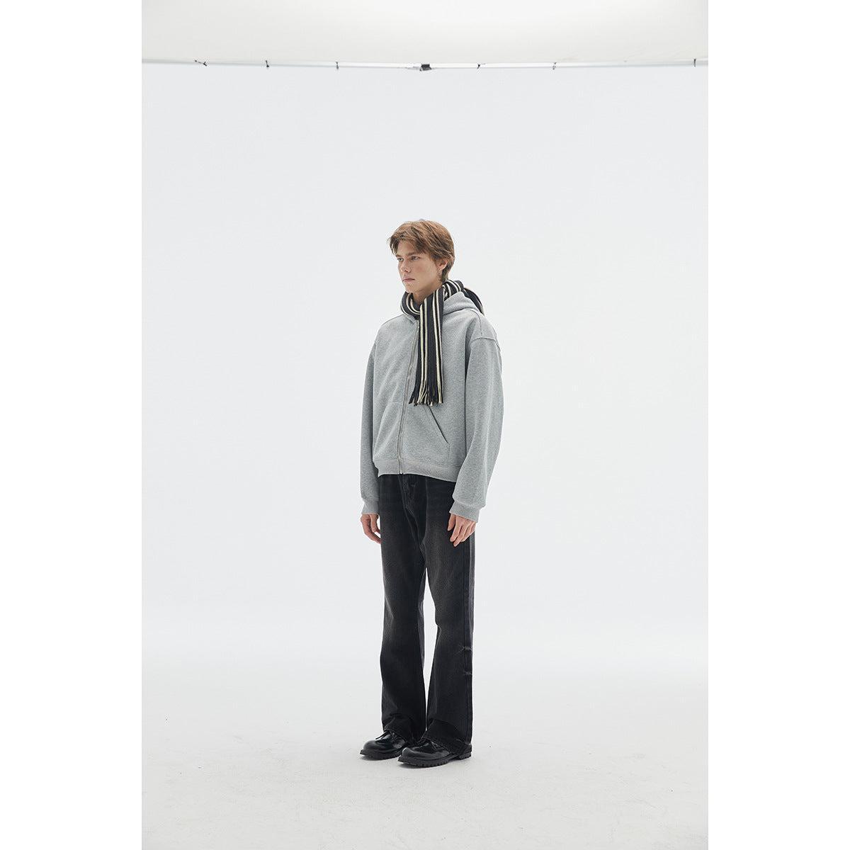 Model wearing a light gray zip-up hoodie with a black-and-cream striped scarf and dark trousers.