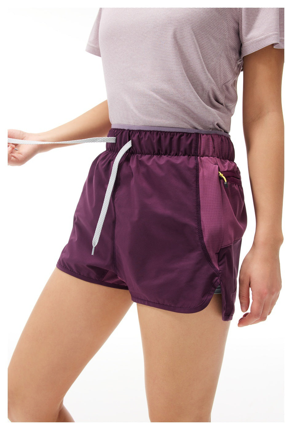 Person wearing dark purple shorts with white drawstring and side zip pocket, with a light mauve top, cropped view