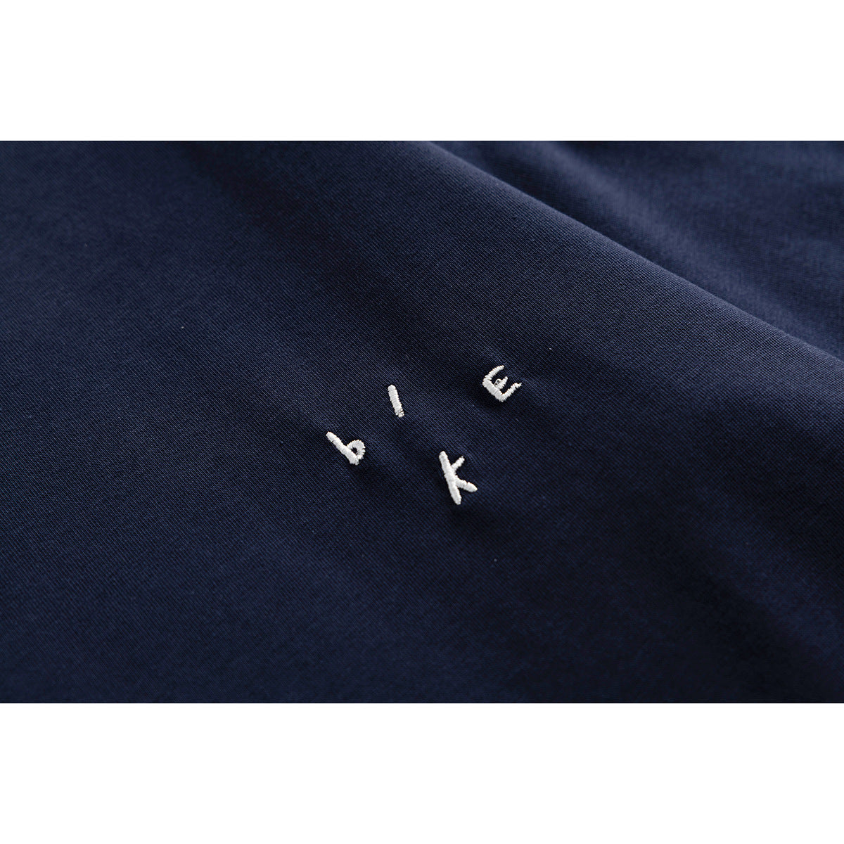 Close-up of small white embroidered lettering on navy T-shirt fabric.