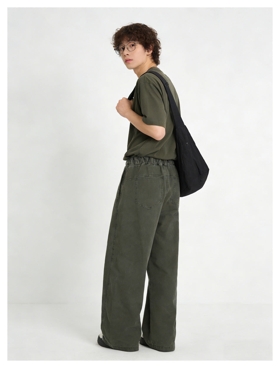 Model in army green wide-leg pants seen from behind, with elastic waistband, back pocket and black shoulder bag