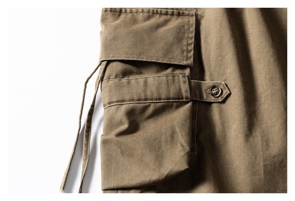 Close-up of a khaki-brown cargo pocket with a buttoned tab and dangling drawcords.