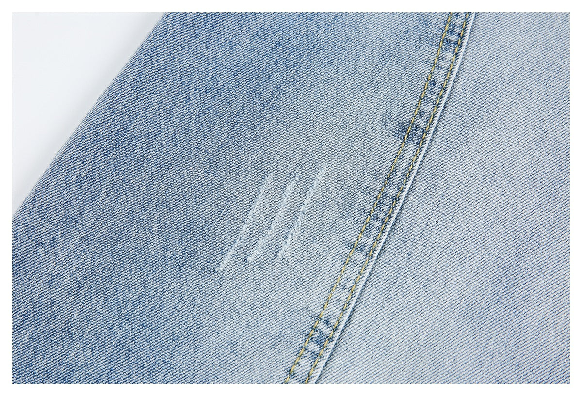 Close-up of light blue denim showing a faint distressed mark beside a yellow-stitched seam.