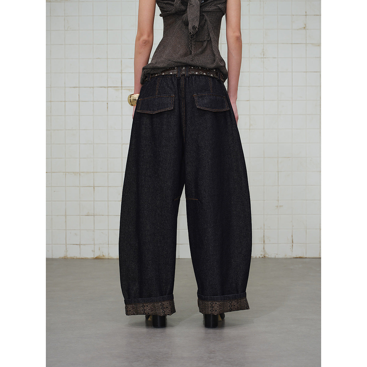 Rear view of a model wearing very wide dark indigo jeans with two back pockets and patterned cuffs.