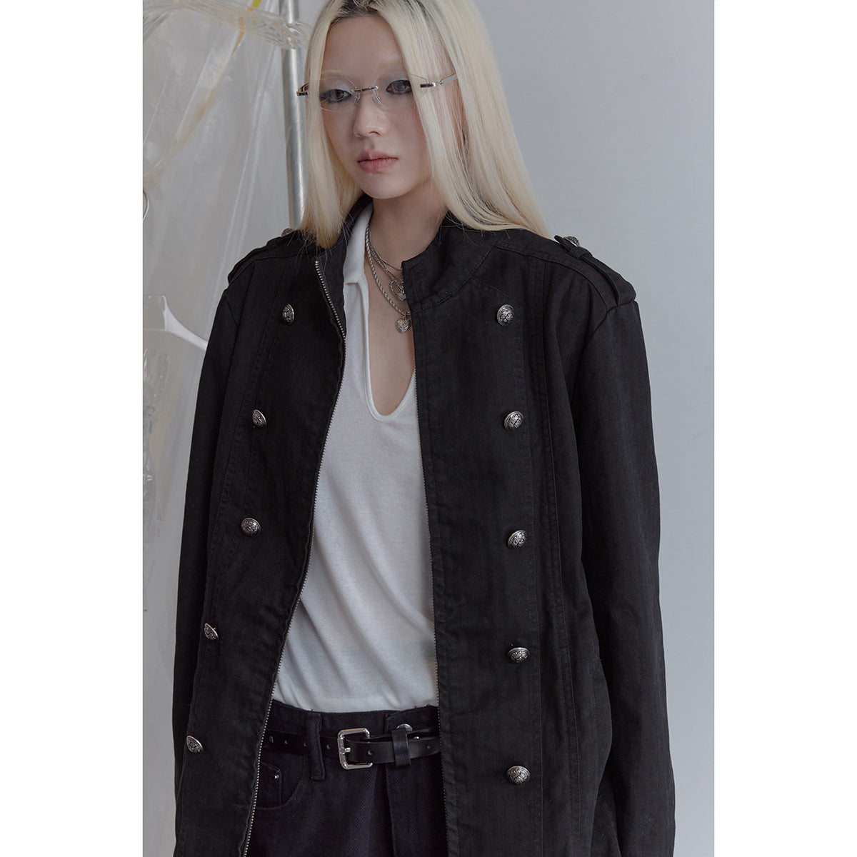 Model wearing a black stand-collar jacket with silver double-breasted buttons, open over a white top.