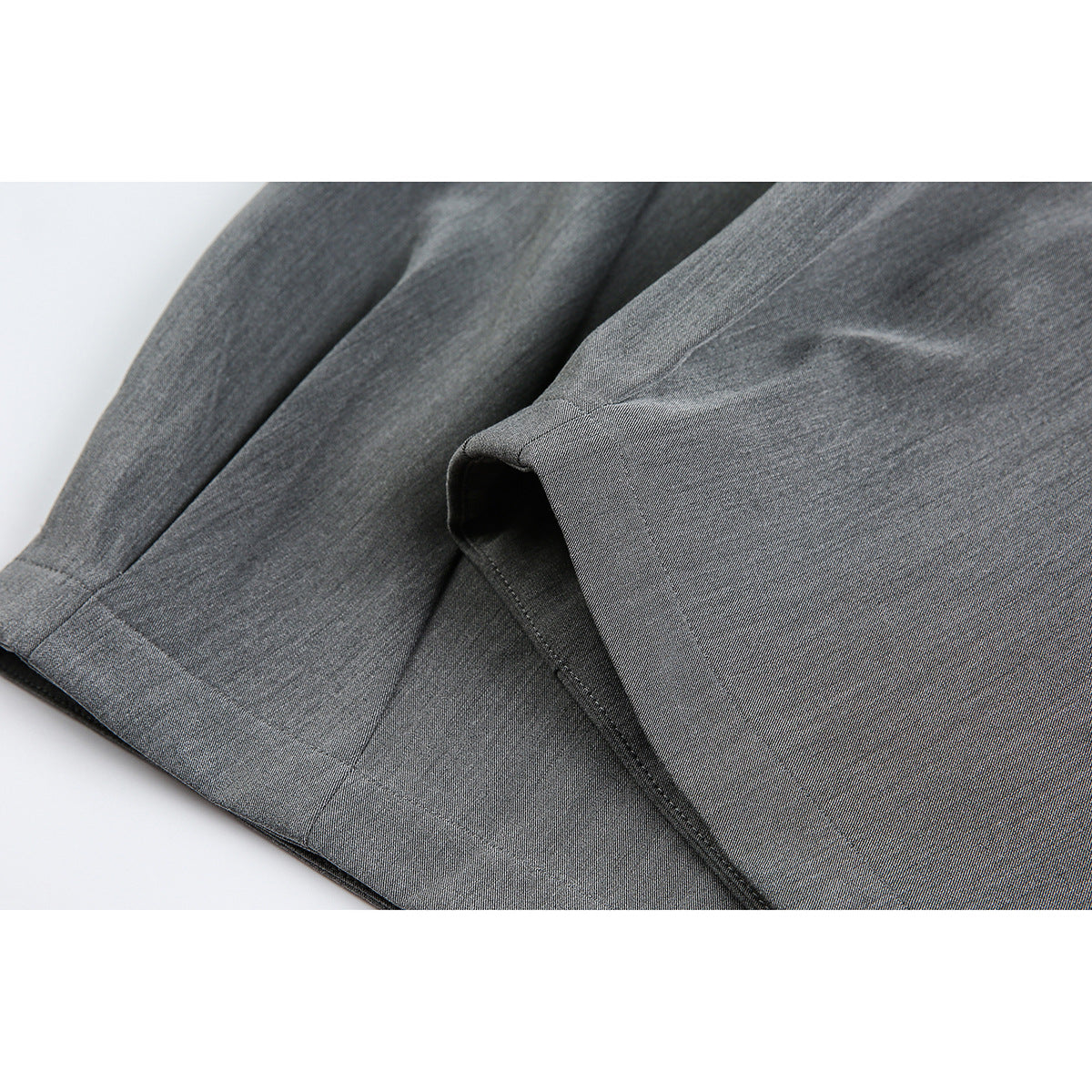 Close-up of the stitched hems and wide legs of gray trousers laid over black trousers.