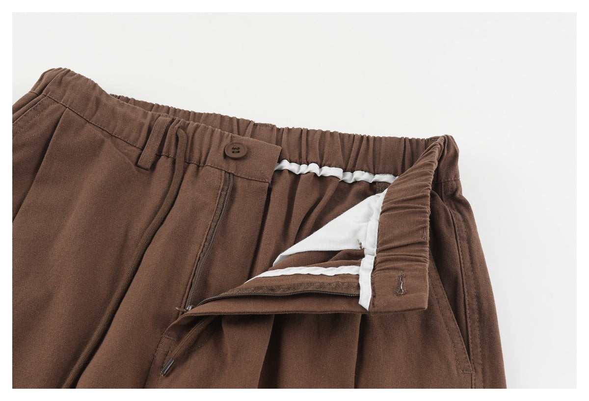 Close-up of brown trousers with the waistband opened to show the fly zipper and white inner facing.