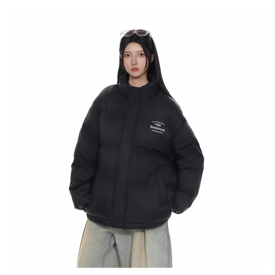Model wearing a zipped black puffer jacket with a high collar, front pockets, and small white chest lettering.