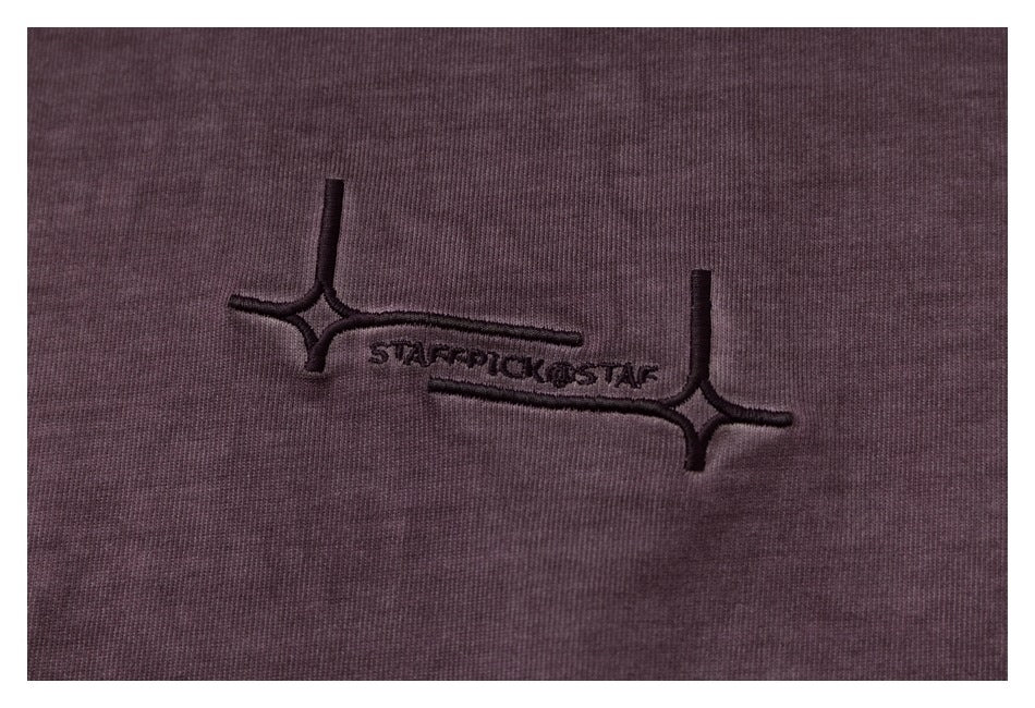Close-up of dark embroidered lettering and star-like motifs on dark plum fabric.