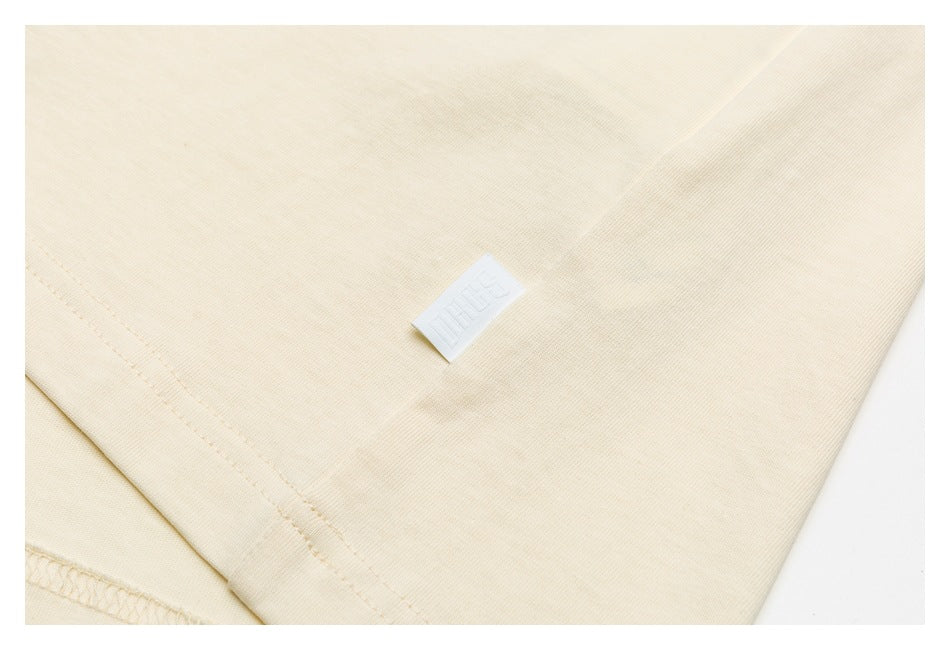 Close-up of cream fabric with a small white woven label and visible seam stitching.
