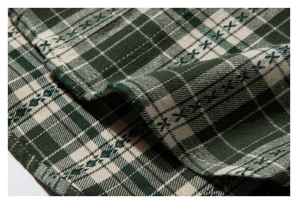 Close-up of folded dark green, cream, and black plaid fabric with fine lines and small decorative motifs.