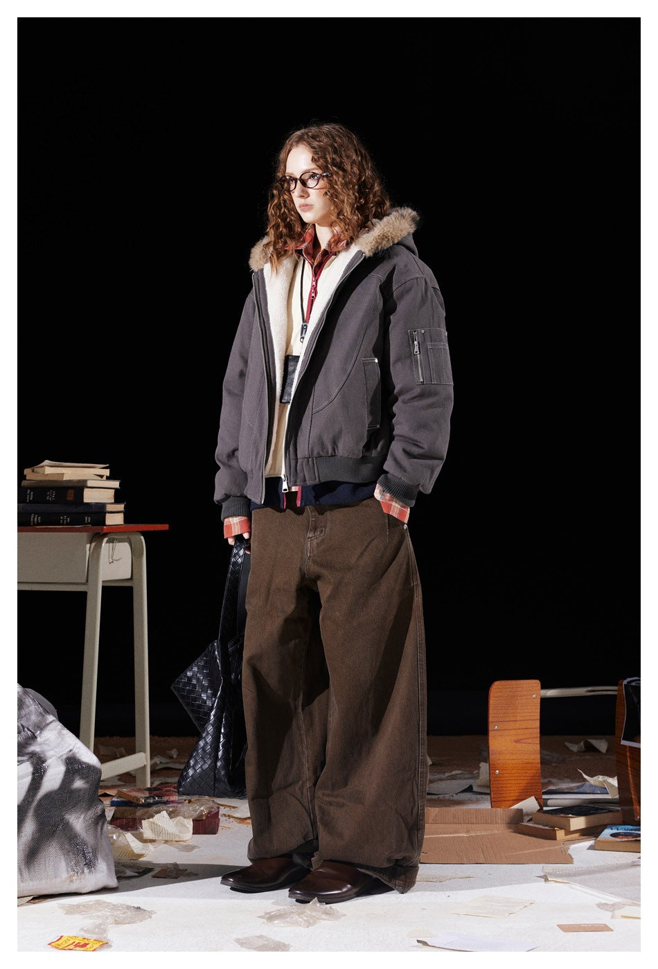 Three-quarter view of a model wearing an open charcoal hooded jacket with cream lining and a fur-trimmed hood.