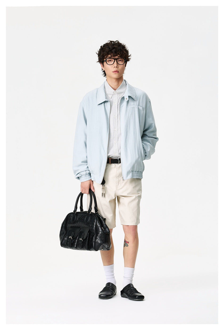 Full-length view of a model wearing a pale blue jacket with a wide collar and elasticated hem, paired with cream shorts.