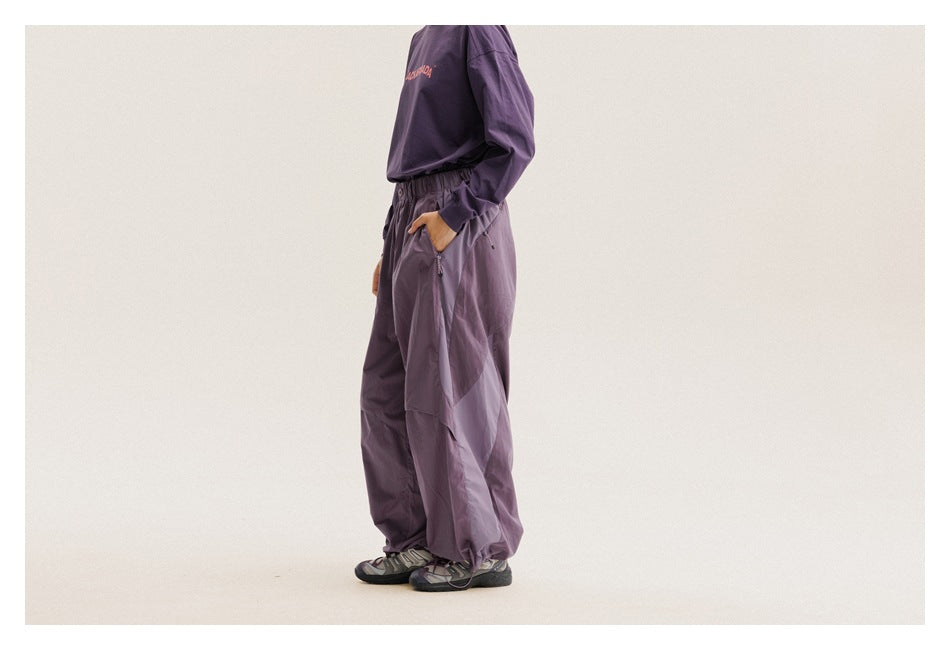 Side view of a model wearing loose purple pants with an elastic waist and color-blocked panels.
