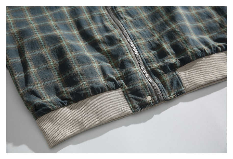 Close-up of the plaid jacket's lower front, showing a central zipper and beige rib-knit hem.