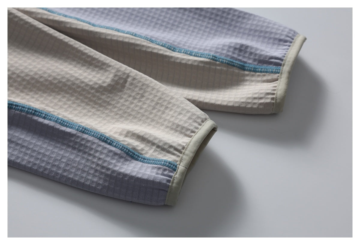 Close-up of gray and off-white textured garment panels with teal seam trim and pale edging at the ends.