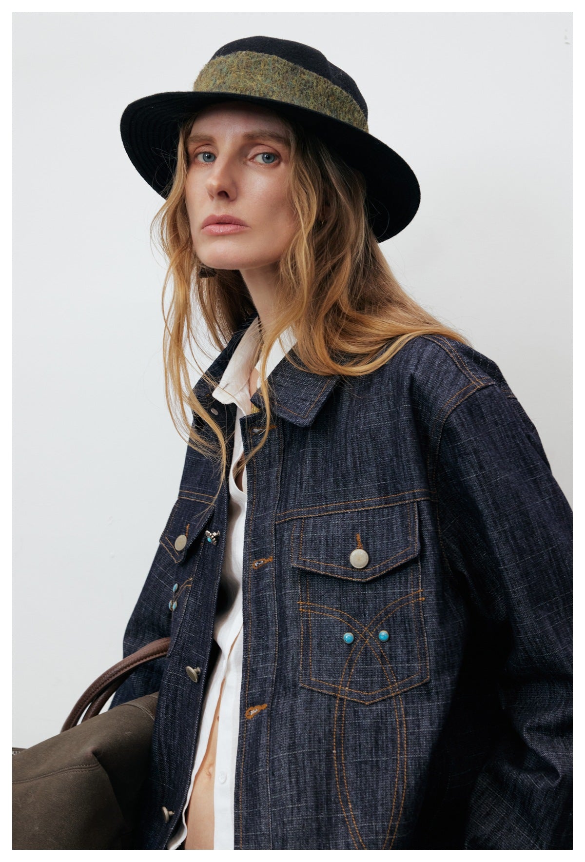 Close-up of a model wearing a dark indigo jacket with contrast stitching, flap pockets, and turquoise accents.
