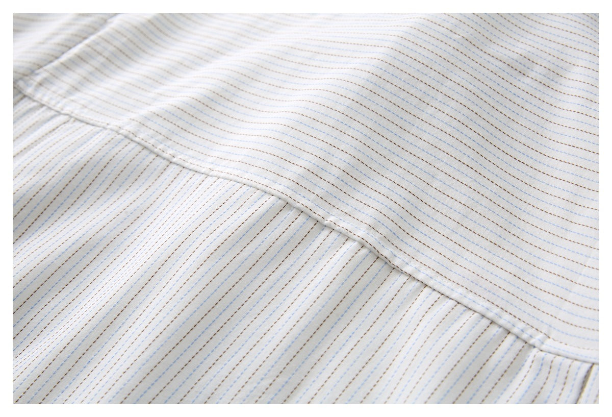 Close-up of white fabric with fine blue and brown dashed stripes and a diagonal stitched seam.