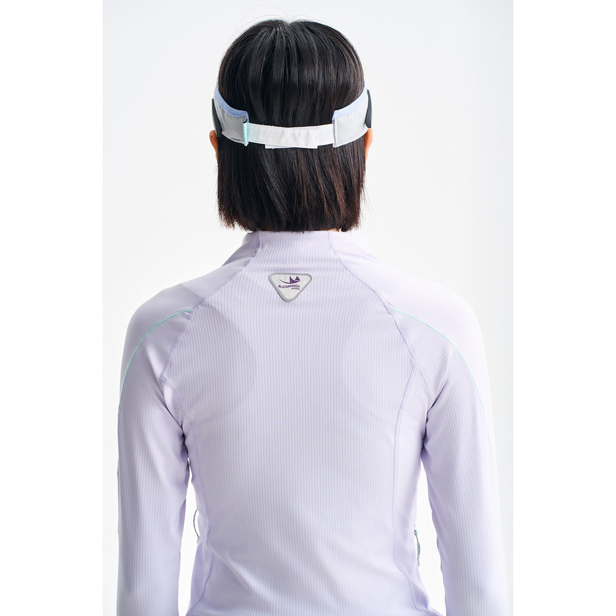 Rear view of a model wearing a pale lilac long-sleeve jacket with aqua piping and a small upper-back emblem.