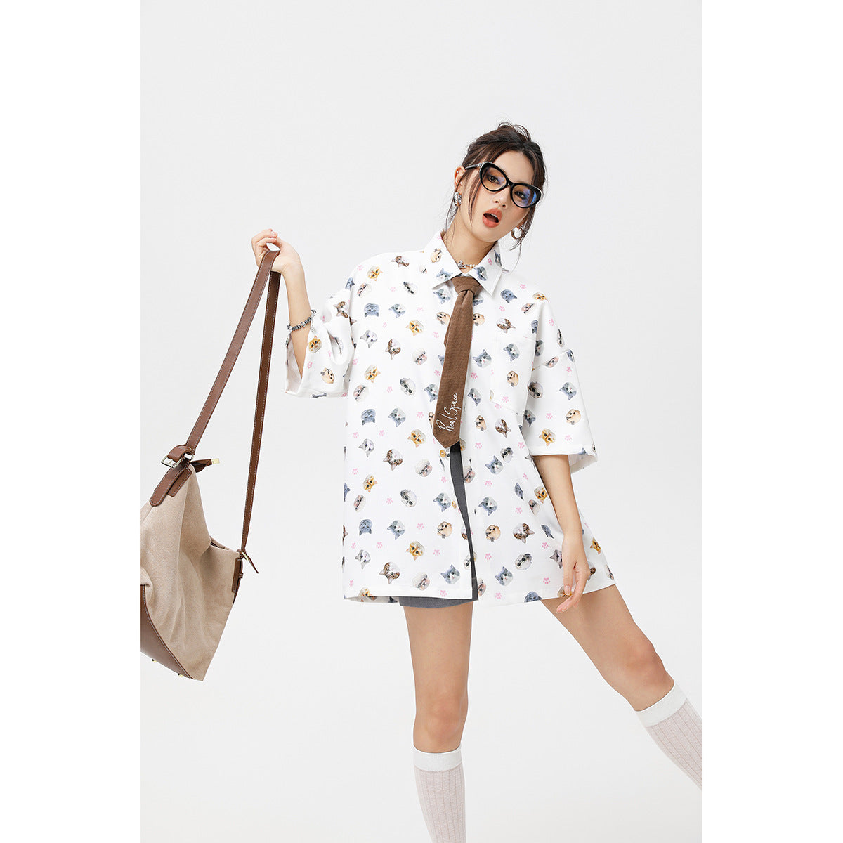 Model wearing an oversized white cat-and-paw-print shirt with a brown tie, shown in a playful pose.