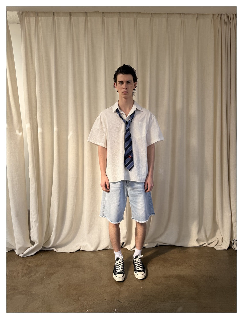 Front view of a model wearing a white short-sleeve collared shirt with chest pocket and striped navy tie.