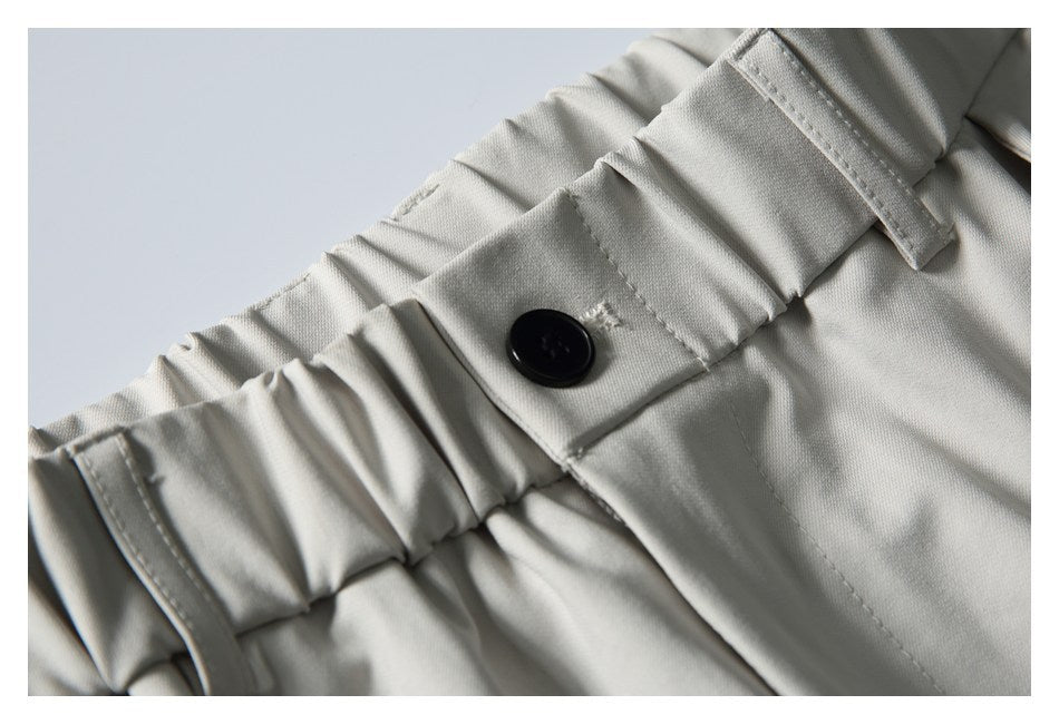 Close-up of the gathered waistband, belt loop, and black button on light gray trousers.