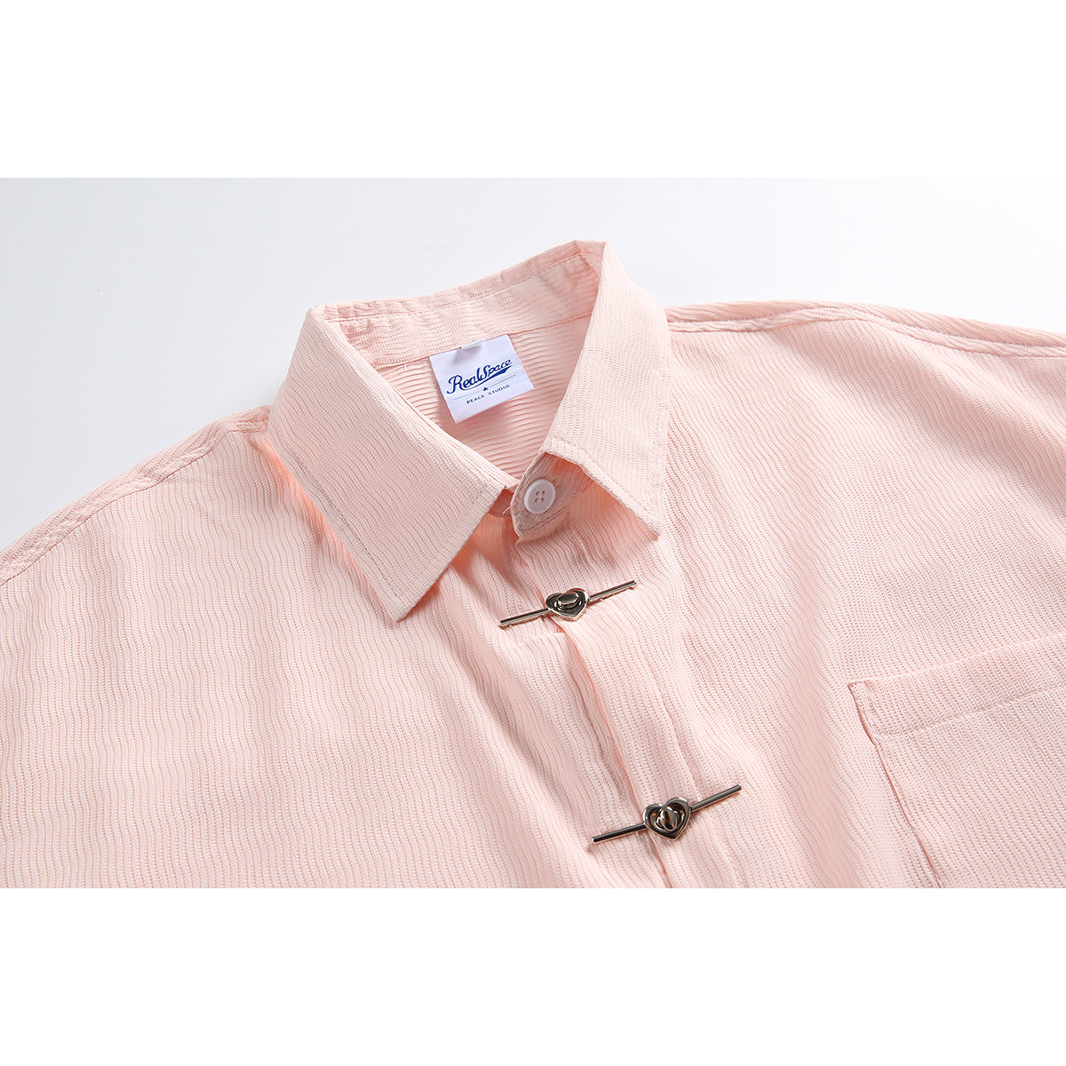 Close-up of a pale pink shirt showing its collar, ribbed texture, chest pocket, metal toggles, and sewn-in neck label.