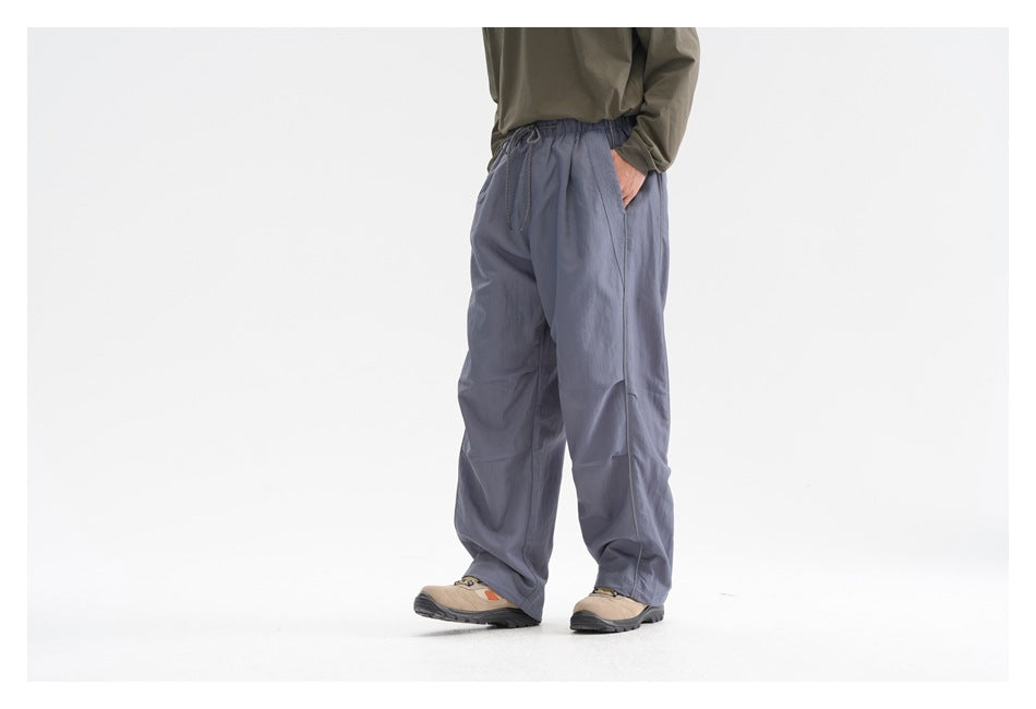 Front view of a model wearing loose slate-blue drawstring trousers with side pockets and hiking shoes.