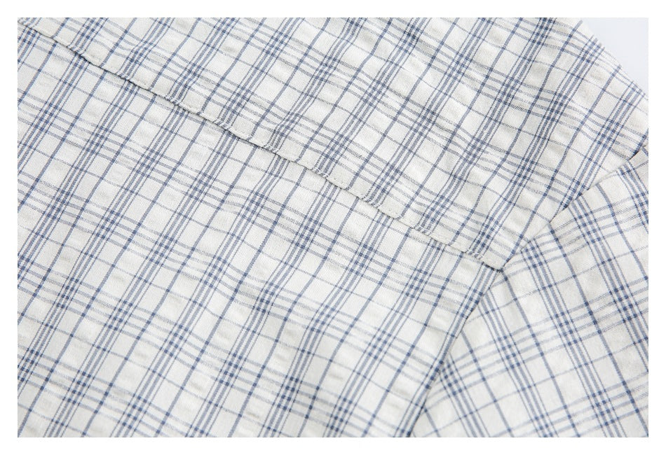 Close-up of a stitched garment seam across cream fabric with a blue-gray plaid pattern.
