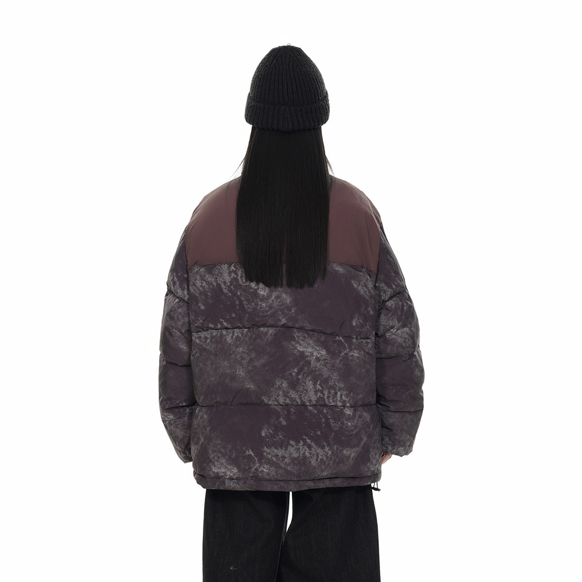 Rear view of a model wearing a dark charcoal marbled puffer jacket with a burgundy upper back panel.
