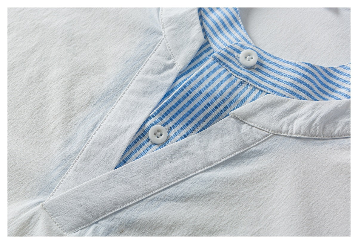 Close-up of a white shirt's blue-and-white striped collar and placket with two white buttons.