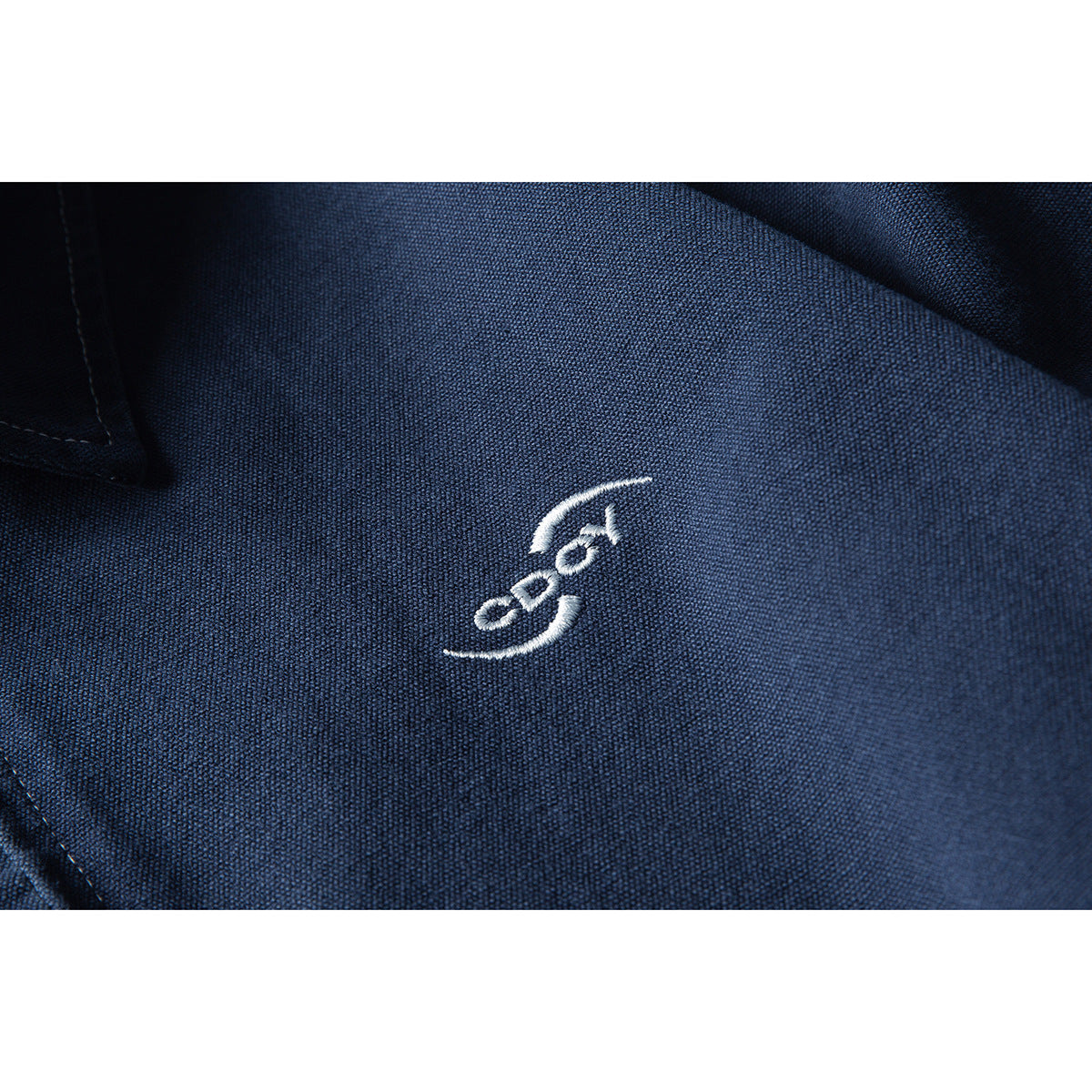 Close-up of a small white embroidered emblem on the textured navy jacket fabric.