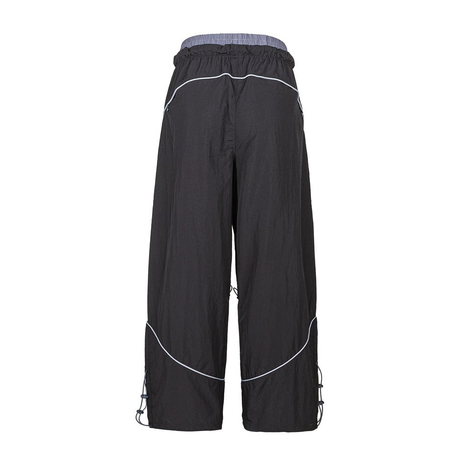 Back view of black wide-leg pants with light contrast piping and adjustable cords at the hems.