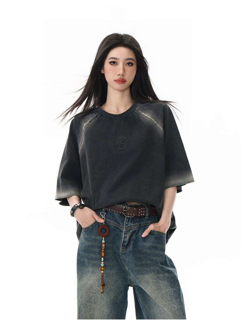 Front view of a model in an oversized charcoal T-shirt with faded gray accents, raglan seams, and a raised chest emblem.
