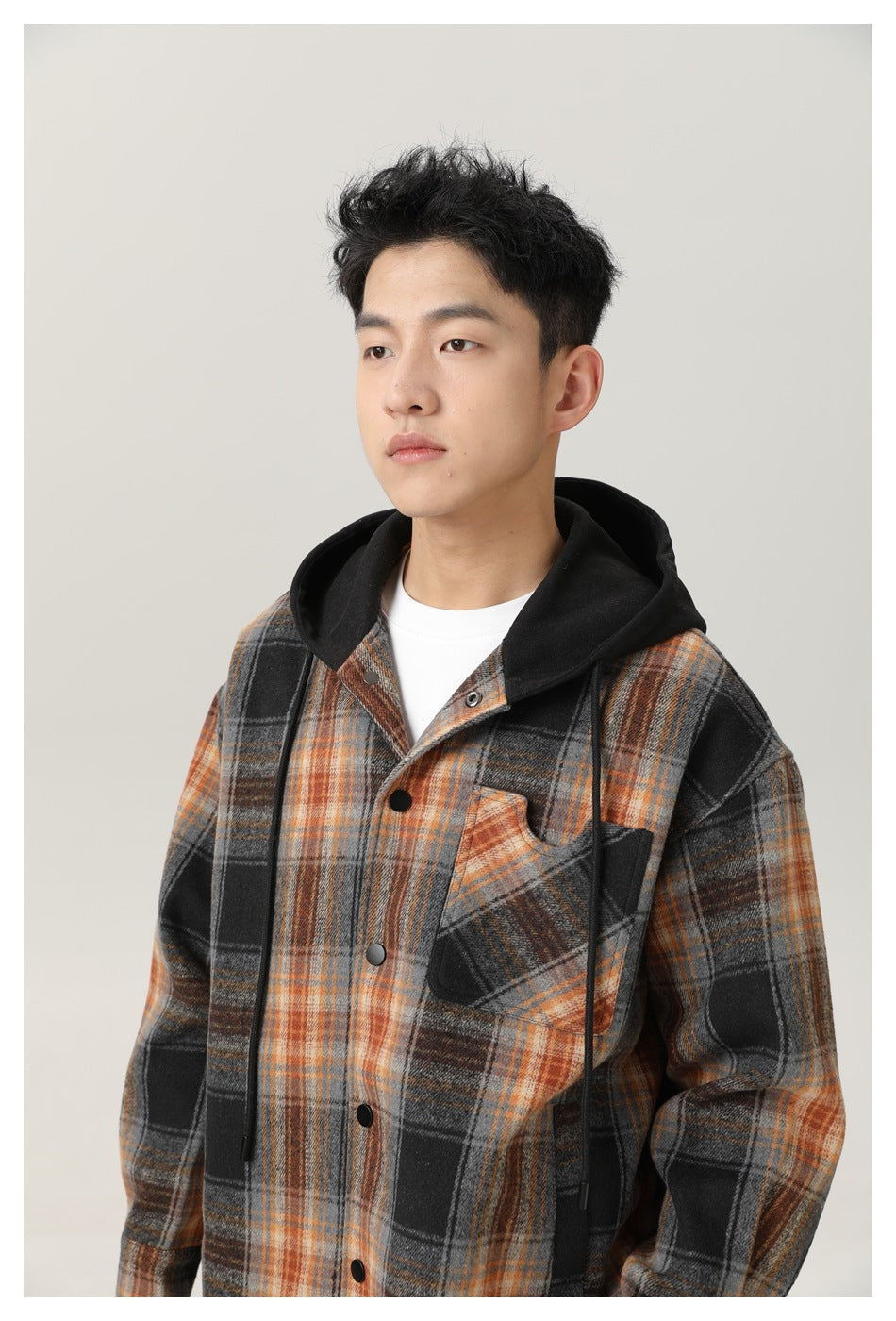 Man wearing a gray, black, and rust plaid button-front hooded shirt jacket with a black hood and chest pocket.