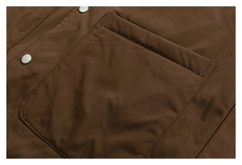 Close-up of a large stitched pocket and snap closures on brown jacket fabric.