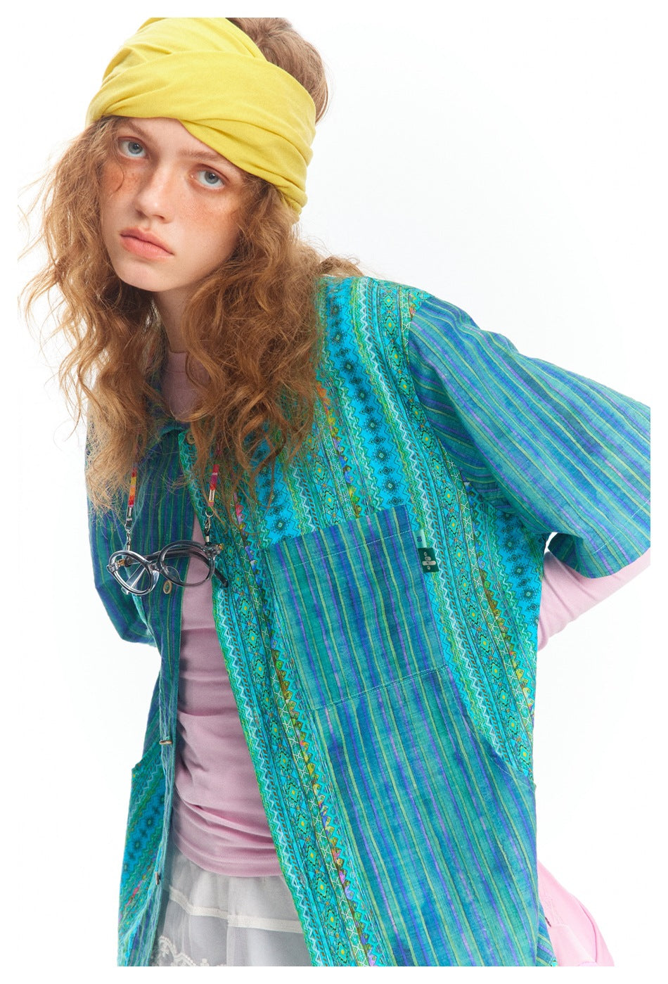 Person wearing the striped patchwork short-sleeve shirt over a pink top with a yellow headscarf, close crop